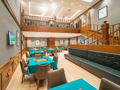 Jasna jadalnia hotelowa z niebieskimi obrusami i nowoczesnymi krzesłami obok drewnianej balustrady.