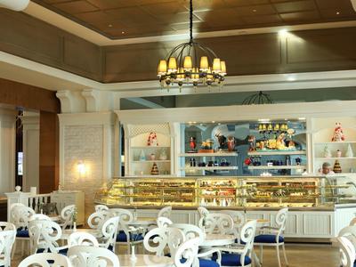 Elegancka kawiarnia z białymi stolikami, dziełami sztuki i podświetlonym ladą w tle.