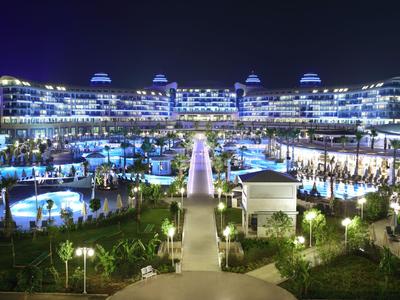 Groot, verlicht hotel met zwembaden en tuinpaden 's nachts.