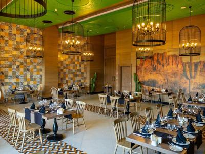 Elegancka restauracja z nowoczesnymi drewnianymi meblami, kolorowymi ścianami i starannie nakrytymi stołami.