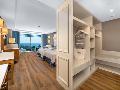 Jasny pokój hotelowy z drewnianą podłogą, dwoma łóżkami i dużym oknem z widokiem na morze.