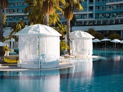 Dwa białe pawilony na brzegu basenu hotelowego z palmami w tle.