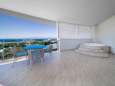 Duży balkon z miejscem do siedzenia i wanną z hydromasażem, w tle widok na morze.