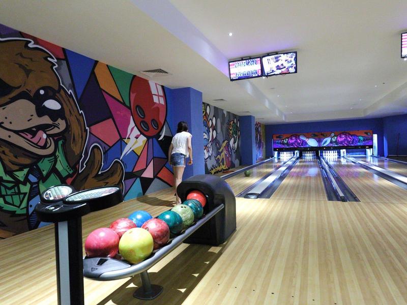 Nowoczesna kręgielnia z kolorowymi kulami do kręgli i muralem niedźwiedzia na ścianie.