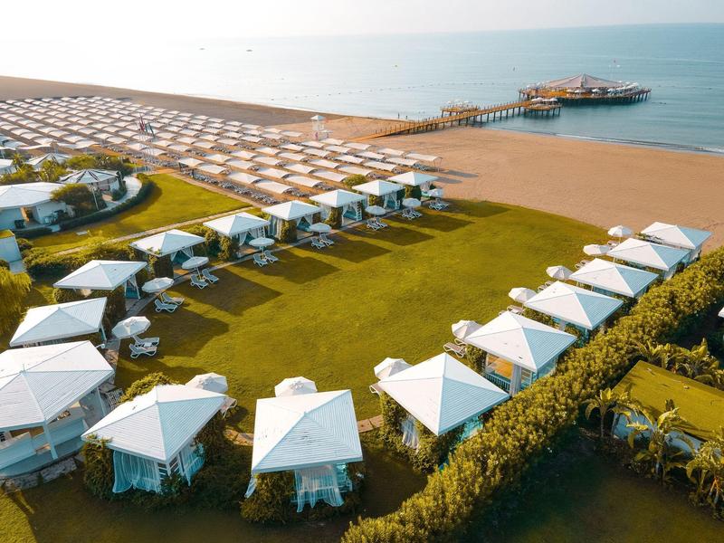 Hotel plażowy z białymi parasolami, leżakami i zielonym trawnikiem nad morzem.