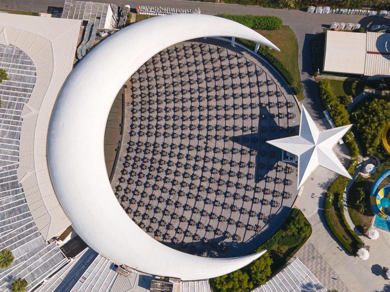 Widok z lotu ptaka na kompleks hotelowy z dużym białym półksiężycem i gwiazdą, obok basenów i zjeżdżalni wodnych.