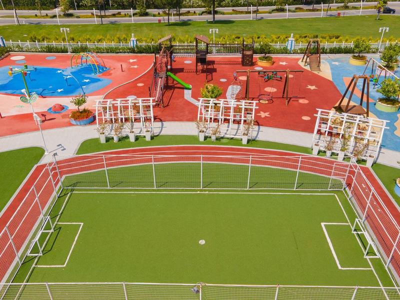 Obiekt sportowy z boiskiem do piłki nożnej, torem biegowym, boiskiem do koszykówki i placem zabaw na zewnątrz.