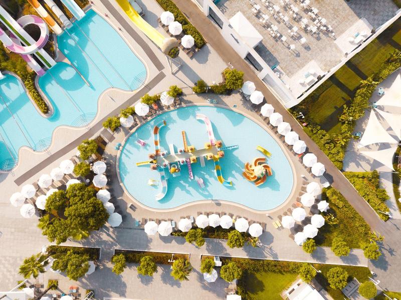 Widok z lotu ptaka na plac zabaw wodny z zjeżdżalniami i parasolami w ośrodku hotelowym.