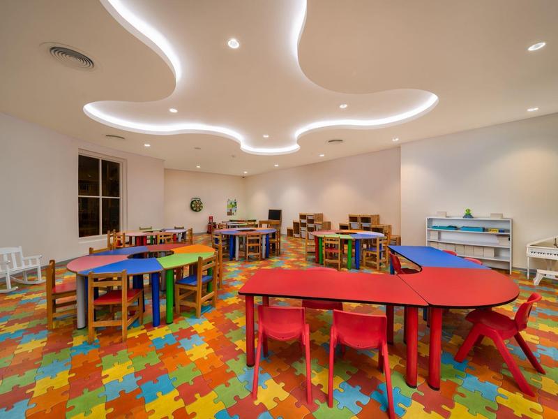 Kolorowy pokój zabaw dla dzieci z stołami, krzesłami i półkami na podłodze z mat puzzlowych.