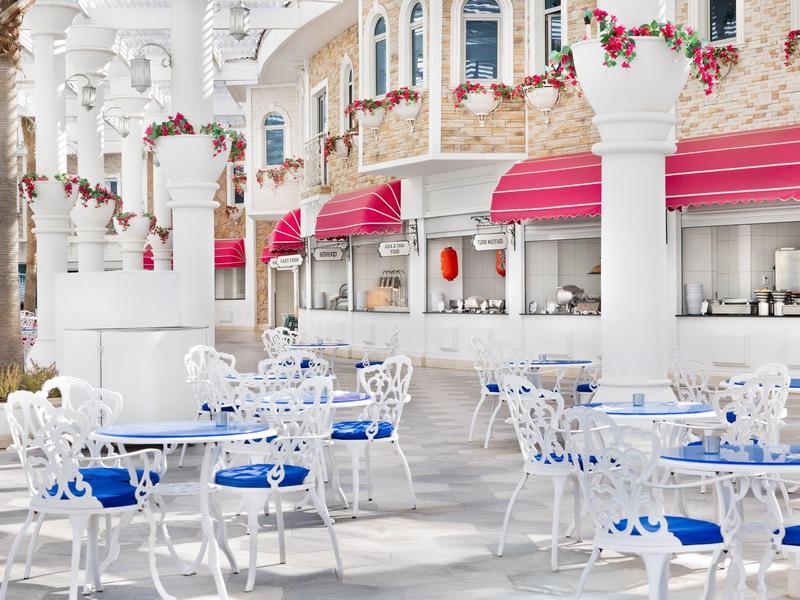 Elegancki teren zewnętrzny hotelu z białymi meblami i niebieskimi poduszkami pod czerwonymi markizami.