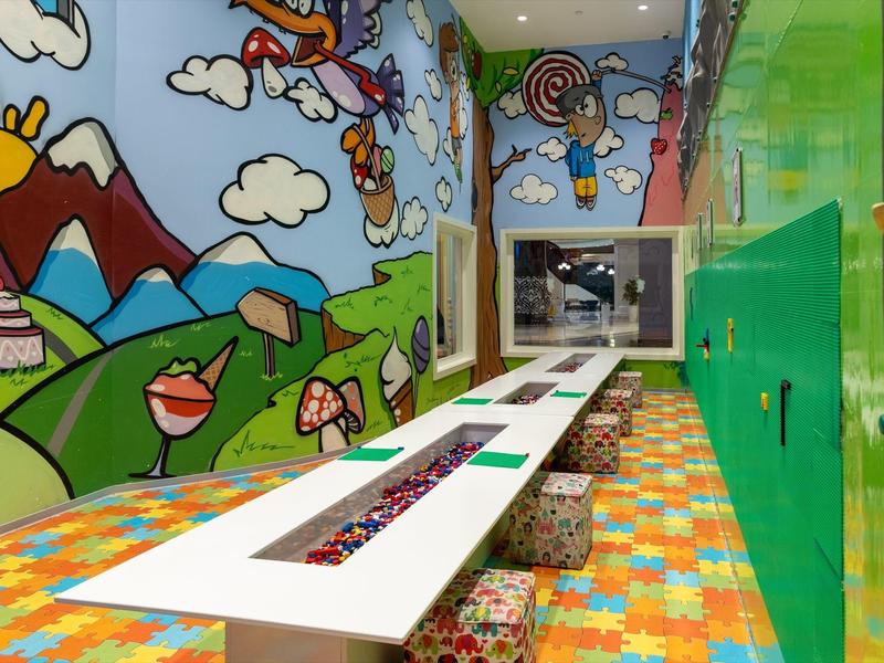 Kolorowy kącik dziecięcy z stołem, siedziskami w formie kostek i ścianą do zabawy w hotelu.