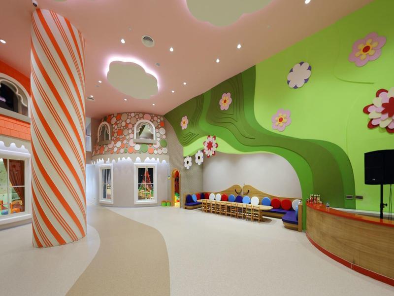 Kolorowy, nowoczesny kącik zabaw w hotelu z zieloną ścianą, ławkami i zabawnymi dekoracjami.