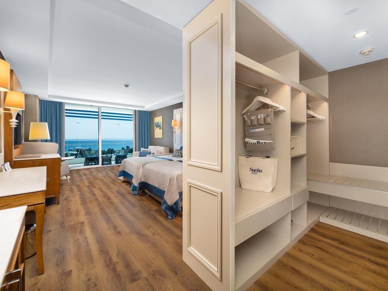 Jasny pokój hotelowy z drewnianą podłogą, dwoma łóżkami i dużym oknem z widokiem na morze.