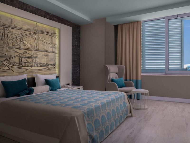 Nowoczesny pokój hotelowy z dużym łóżkiem, fotel i oknem z żaluzjami.