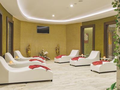 Eleganter Spa-Raum mit weißen Liegen, roten Handtüchern und warmem Licht auf hellen Fliesen.