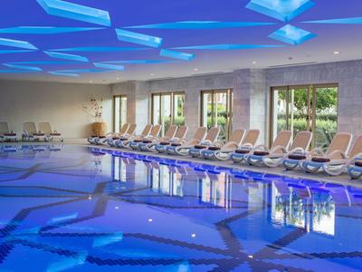 Innenpool mit blauer LED-Beleuchtung, Liegestühlen und großen Fenstern mit Blick ins Grüne.