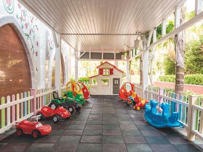 Überdachter Spielbereich mit bunten Kinderfahrzeugen und kleinem Spielhaus auf weichen Matten.