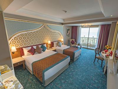 Camera d'hotel con due letti, balcone, vista sul mare, arredata con stile e moquette.