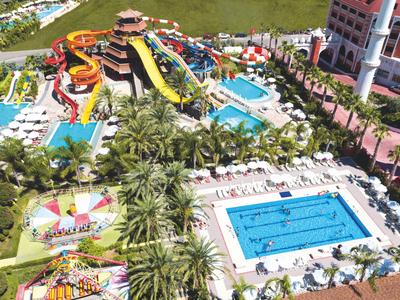 Parco acquatico con piscine, scivoli d'acqua, sdraio e palme in un resort alberghiero.