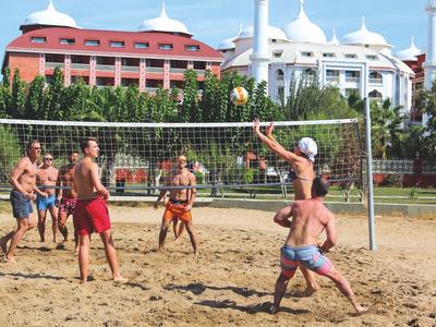 Menschen spielen Volleyball im Sand mit Hotelgebäuden im Hintergrund bei sonnigem Wetter.