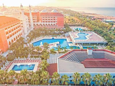 Großes Resort mit mehreren Pools, Palmen, roten Gebäuden und Blick aufs Meer bei Sonnenuntergang.