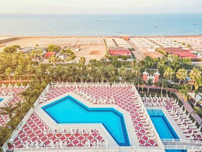 Luftaufnahme von zwei Pools mit blauer Wasserfläche, umgeben von roten Liegestühlen und Palmen.