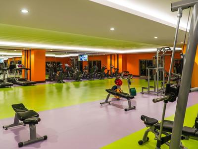 Heller Fitnessraum mit grün-lila Boden, Kraftgeräten und Spiegelwand an orangen Wänden.