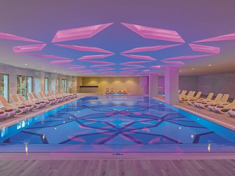 Innenpool mit blauem Wasser und rosa-lila Deckenbeleuchtung in einem modernen Spa-Bereich