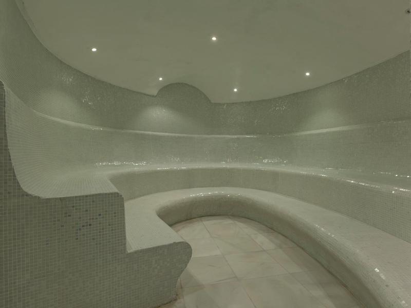 Runder Dampfraum mit glatten, hellen Steinbänken und eingelassener Deckenbeleuchtung.