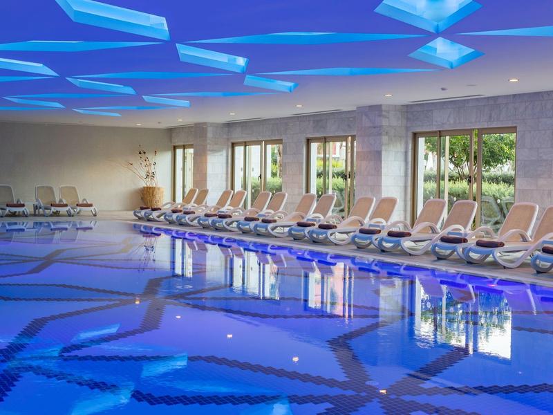 Moderner Innenpool mit blauer Beleuchtung und Liegestühlen an den Fenstern.