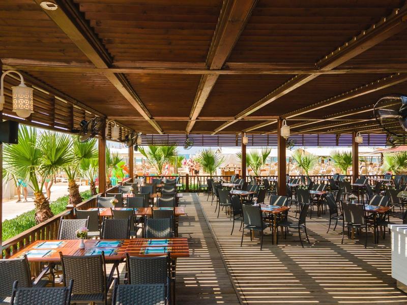 Überdachte Terrasse mit Tischen und Stühlen in einem Urlaubshotelrestaurant.