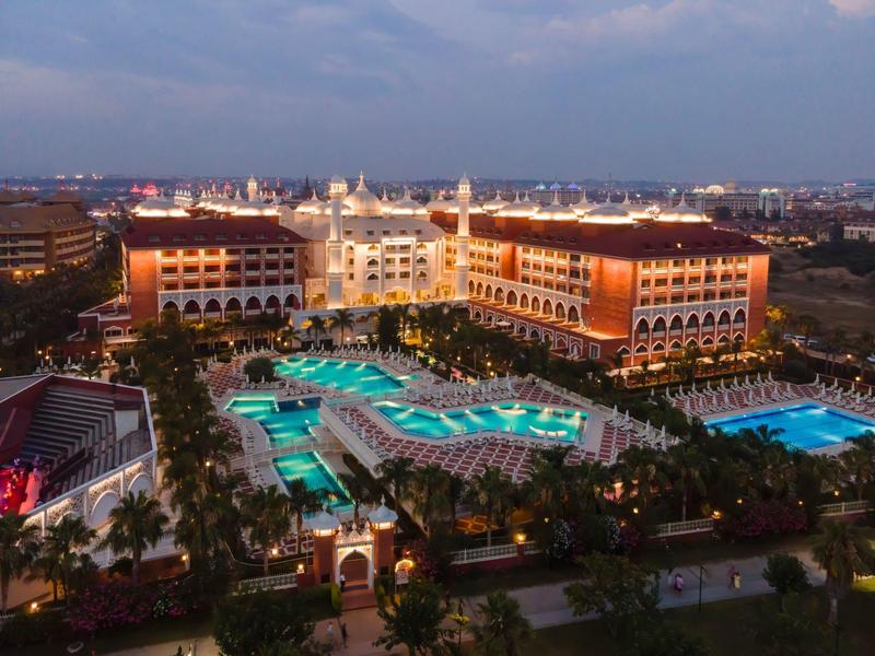 Abendaufnahme eines großen Hotels mit beleuchteten Pools und Palmen.