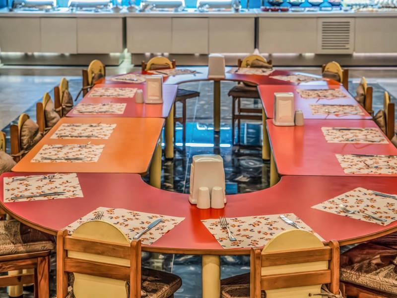 Restaurant mit rotem T-förmigem Tisch, Holzstühlen und bunten Platzsets in einem Hotel