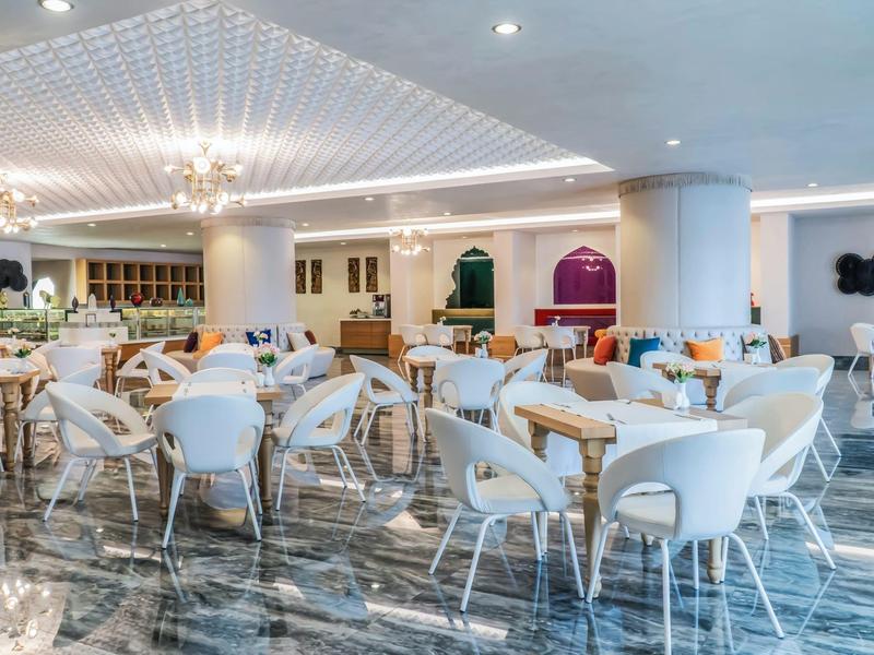 Großer, heller Hotelrestaurantbereich mit weißen Stühlen und Marmorfußboden.