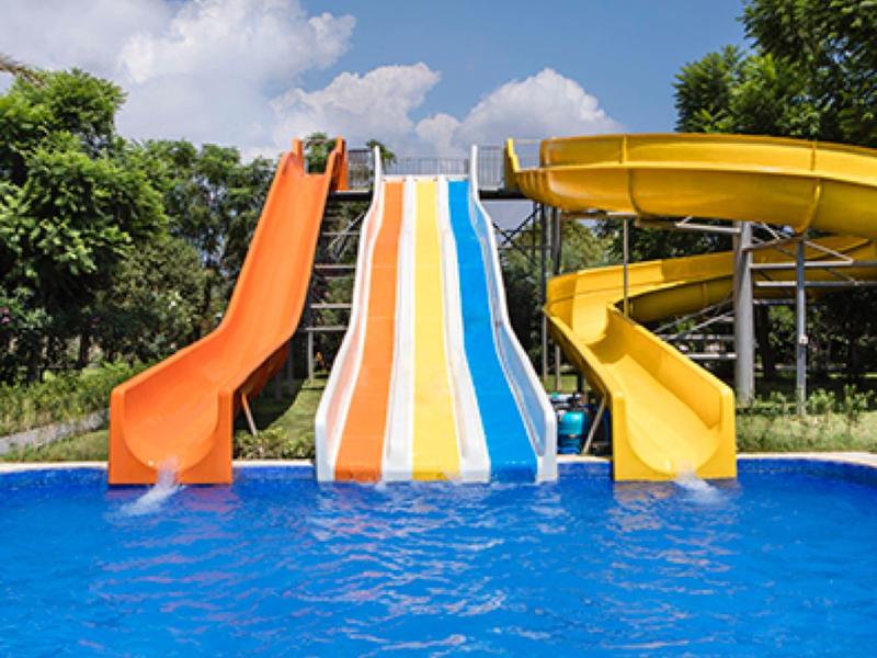 Tres toboganes de agua de colores desembocan en una piscina, rodeados de árboles y cielo azul.