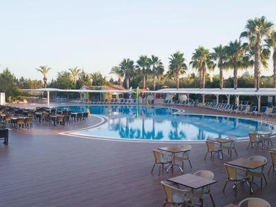 Grande piscina all'aperto con tavoli rotondi e sedie sotto palme in un resort.