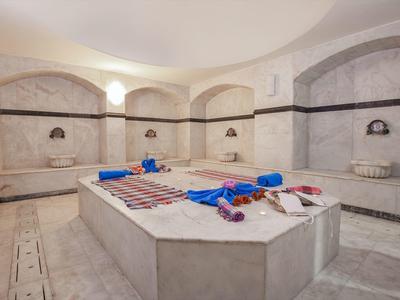 Ampio hammam ben illuminato con pareti e panche in marmo, asciugamani e oli sulla lastra centrale per massaggi.