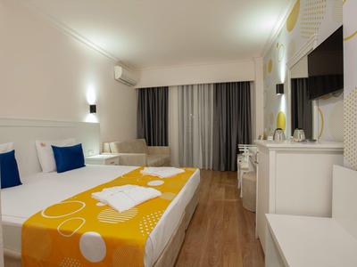 Camera d'hotel moderna con letto matrimoniale, copriletto arancione e bianco e TV a parete.