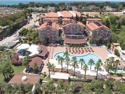 Widok z powietrza na duży hotel z basenem, parasolami i palmami w zielonym otoczeniu.