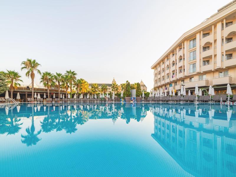 Grande piscina dell'hotel con ombrelloni e palme sotto un cielo sereno.