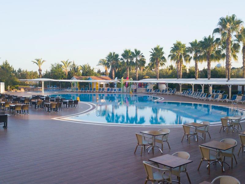 Grande piscina all'aperto con tavoli rotondi e sedie sotto palme in un resort.