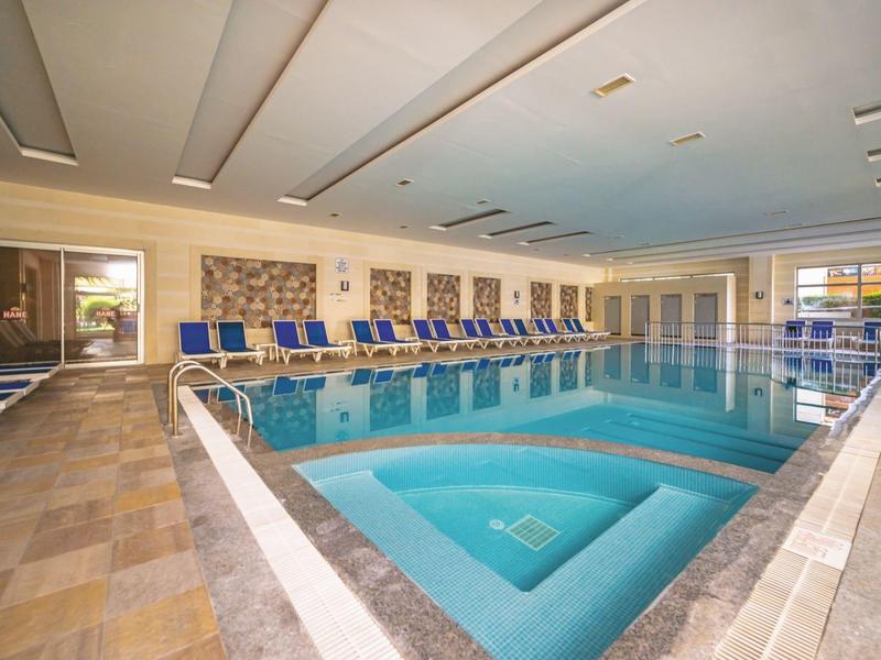 Piscina interna con vasca idromassaggio annessa e lettini in un ambiente luminoso e moderno.