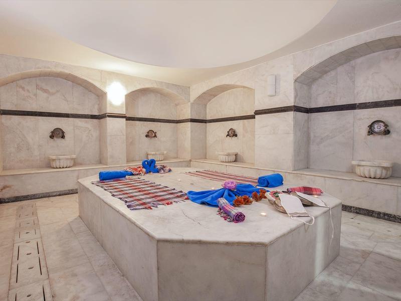 Ampio hammam ben illuminato con pareti e panche in marmo, asciugamani e oli sulla lastra centrale per massaggi.