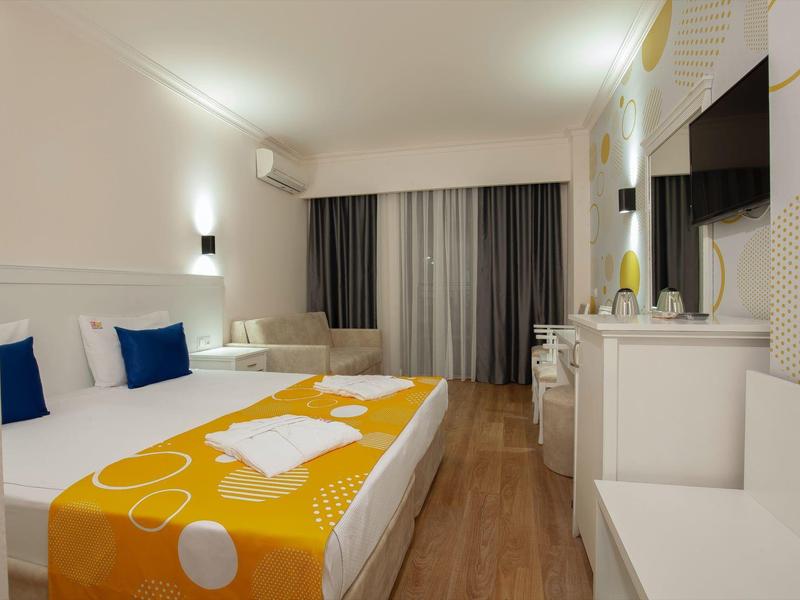 Camera d'hotel moderna con letto matrimoniale, copriletto arancione e bianco e TV a parete.