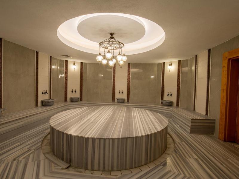 Sala hammam rotonda moderna con panche in marmo e piattaforma centrale sotto una luce a soffitto.