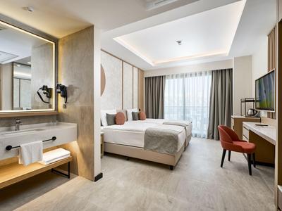Camera d'hotel moderna con letto grande, scrivania, sedia e bagno aperto con lavabo.
