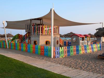 Bunter Kinderspielplatz mit einem überdachten Klettergerüst und Zaun, umgeben von Sand und Rasen.