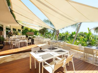 Sonnige Terrasse eines Hotels mit weißen Tischen und Stühlen unter schattenspendenden Segeln