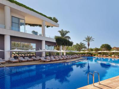 Hotel moderno con grande piscina e lettini in una giornata di sole.