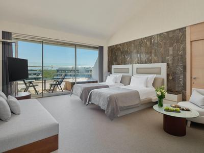 Helles Hotelzimmer mit zwei Einzelbetten, Sofa und großem Fenster mit Blick auf eine Terrasse.